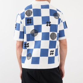 Model wearing Wax London Porto Printed Cardigan in ecru and blue checkerboard with geometric print, short sleeves, polo collar, back view.
