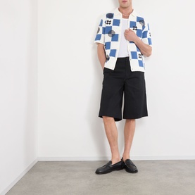 Model wearing Wax London Porto Printed Cardigan in ecru and blue check knit, styled with black shorts and leather loafers