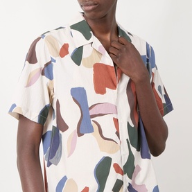 Model wearing Wax London Didcot Abstract Print Shirt in ecru and multi, with camp collar and short sleeves, hand raised to chest.