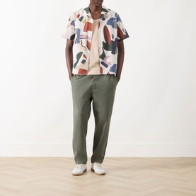 Model wearing Wax London Didcot Abstract Print Shirt in ecru/multi with camp collar, styled with olive trousers and white trainers.