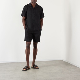 Model wearing Wax London Didcot Linen Bowling Shirt in black, styled with matching black shorts and brown leather sandals.