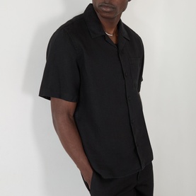 Model wearing Wax London Didcot Linen Bowling Shirt in black with notched collar, chest pocket, and short sleeves, styled with a gold chain.