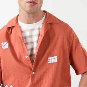 Model wearing Wax London Didcot Scribble Casual Shirt in terracotta, short sleeves, spread collar, squiggle applique, styled over striped tee
