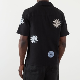 Model wearing Wax London Ditcot Embellished Bowling Shirt in black with multi-coloured snowflake embroidery, short sleeves, back view.