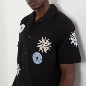Model wearing Wax London Ditcot Embellished Bowling Shirt in black with floral snowflake embroidery in white and blue, short sleeves, notched collar