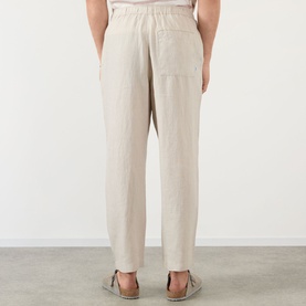 Model wearing Wax London Kurt Linen Relaxed Fit Trousers in beige, shown from behind, with rear patch pockets and elasticated waistband visible.