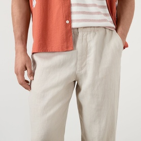 Model wearing Wax London Kurt Linen Relaxed Fit Trousers in beige, elasticated waistband, styled with a coral linen shirt and striped tee.
