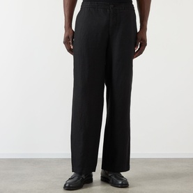 Model wearing Wax London Glencoe Linen Trousers in black, mid-rise straight leg with button fastenings, styled with black leather shoes.