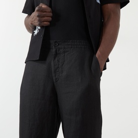 Model wearing Wax London Glencoe Linen Trousers in black, mid-rise straight leg with side pockets, styled with a black short-sleeve shirt.