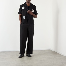 Model wearing Wax London Glencoe Linen Trousers in black, straight leg, styled with a matching black embroidered shirt and black loafers.