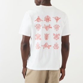 Model wearing Wax London Dean Logo Embroidery T-Shirt in ecru, back view showing rust floral motif grid embroidery, styled with beige trousers.