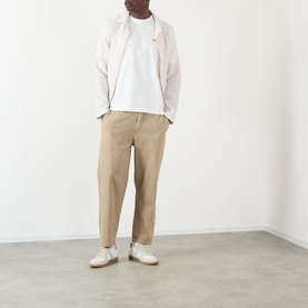 Model wearing Wax London Dean Logo Embroidery T-Shirt in Ecru, styled with a light pink overshirt, beige trousers and white trainers.