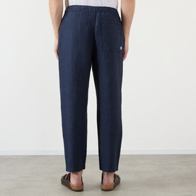 Model wearing Wax London navy linen casual trousers, rear view, shown with brown leather sandals.