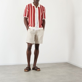 Model wearing Wax London Kurt Linen Shorts in beige, styled with a red striped shirt and brown sandals.