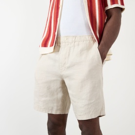 Model wearing Wax London Kurt Linen Shorts in beige, styled with a red and white striped shirt. Mid-rise with side pockets visible.