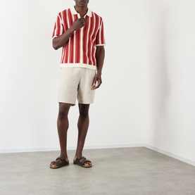 Model wearing Wax London Kurt Linen Shorts in beige, styled with a red striped polo shirt and brown leather sandals.