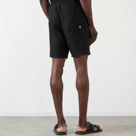 Model wearing Wax London Kurt Linen Shorts in black, rear view. Styled with black slide sandals.