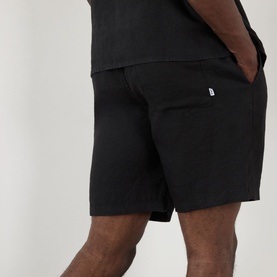 Model wearing Wax London Kurt Linen Shorts in black, mid-rise straight leg style with side pockets, styled with a black t-shirt.