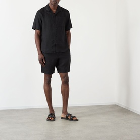 Model wearing Wax London Kurt Linen Shorts in black, styled with a matching black linen shirt and black sandals.