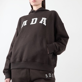 Model wearing Adanola ADA Logo Oversized Hoodie in Coffee Bean, with matching sweatpants. Features large ADA lettering and kangaroo pocket.