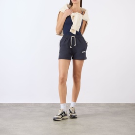 Model wearing Adanola Midnight Blue shorts with white drawstring, styled with cream sweatshirt tied at shoulders and grey trainers.