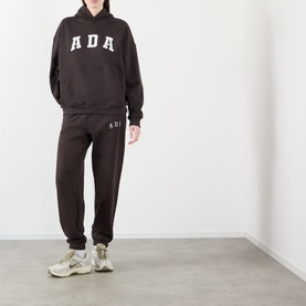 Model wearing Adanola ADA Logo Sweatpants in Coffee Bean, slim-leg with cuffed ankles, styled with matching hoodie and cream trainers