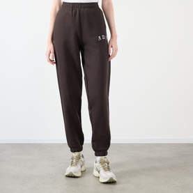Model wearing Adanola ADA Logo Sweatpants in Coffee Bean, slim-leg with cuffed ankles and chest logo, styled with white chunky trainers