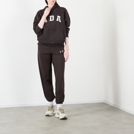 Model wearing Adanola ADA Logo Sweatpants in Coffee Bean, slim-leg cuffed style, styled with matching sweatshirt and white trainers.