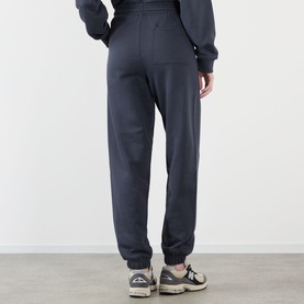 Model wearing Adanola ADA Logo Sweatpants in Midnight Blue, slim-leg with cuffed ankles, styled with grey trainers, rear view.