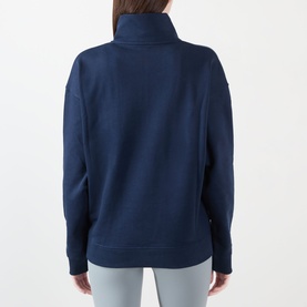 Model wearing Adanola Varsity Logo Half-Zip Sweatshirt in Navy Blue, rear view, funnel neck, dropped shoulders, paired with light grey leggings.