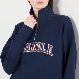 Model wearing Adanola Varsity Logo Half-Zip Sweatshirt in navy blue with burgundy logo, funnel neck, half-zip placket detail shown close up.