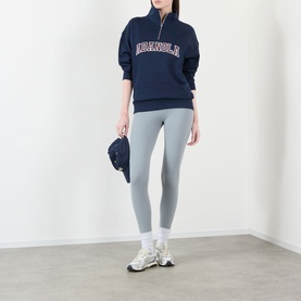 Model wearing Adanola Varsity Logo Half-Zip Sweatshirt in navy blue/burgundy with grey leggings and white trainers.