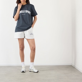 Model wearing Adanola ADA Sport Oversized Logo T-Shirt in Midnight Blue with white logo, styled with light grey shorts and white trainers.