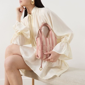 Model carrying Chlo&eacute; P777 Stripy Mini Tote Bag in Nougat; pink striped canvas, gold-tone hardware, top handles, styled with cream dress