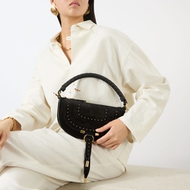 Model carrying Chloe Marcie Mini Crossbody Bag in black suede with gold-tone hardware and stud detailing, styled with cream oversized shirt and