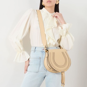 Model carrying Chlo&eacute; Marcie Saddle Crossbody Bag in Petal Beige, grained leather, gold-toned hardware, worn crossbody with white ruffled blouse and