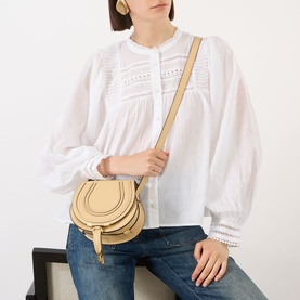 Model carrying Chloe Marcie Small Saddle Crossbody Bag in Petal Beige, grained leather, gold-toned hardware, worn crossbody with white blouse and