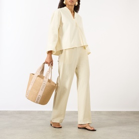Model carrying Chlo&eacute; Woody Large Basket Tote Bag in Blushy Beige with logo tape detail and carry handles, styled with cream wide-leg trousers and