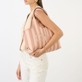 Model carrying Chloe Stripy East-West Tote Bag in Nougat, pink stripe jacquard, gold-tone hardware, top handle, styled with white jeans