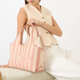 Model carrying Chlo&eacute; Stripy East-West Tote Bag in Nougat, pink stripe jacquard with gold-tone hardware and top handles, styled with cream vest and