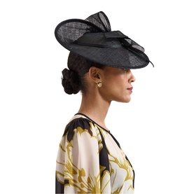 Model with Phase Eight black sinamay fascinator hat featuring bow and feather detail, styled with floral dress and gold earrings