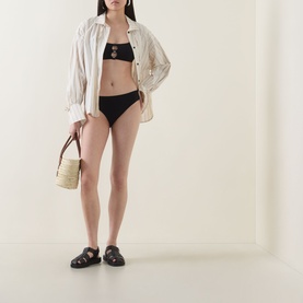 Model wearing Eres Clap Cut-Out Classic Bikini Briefs in Noir, mid-rise high leg, styled with white shirt, straw bag and black sandals