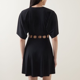 Model wearing Eres Connection Cut-Out Beach Dress in Noir, shown from behind with cut-out waist detailing and flared mini skirt