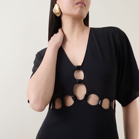 Model wearing Eres Connection Cut-Out Beach Dress in Noir, featuring V-neckline, short sleeves and circular cut-out detailing. Gold drop earrings