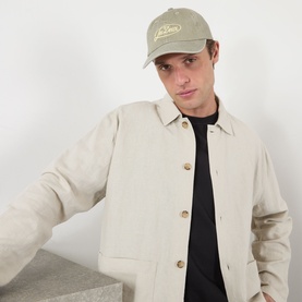 Model with Les Deux Logo Dad Cap in Laurel Oak Sand, six-panel cotton cap with embroidered logo, styled with a cream jacket and black top.