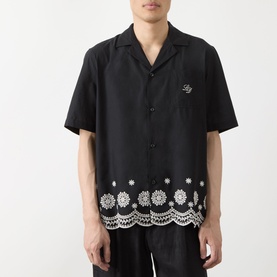 Model wearing Les Deux Border Embroidered Shirt in black with white floral crochet-style embroidered hem, camp collar, short sleeves, styled with