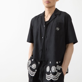 Model wearing Les Deux Border Embroidered Shirt in tap shoe black with camp collar, scalloped hem, and white embroidery detail, styled with matching