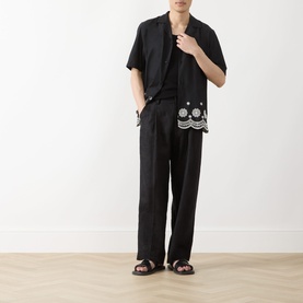 Model wearing Les Deux Border Embroidered Shirt in tap shoe black with scalloped hem, styled with black trousers and sandals.
