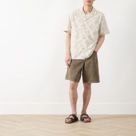 Model wearing Les Deux Dahlia Jacquard Shirt in light sand with camp collar and floral pattern, styled with khaki shorts and brown sandals.