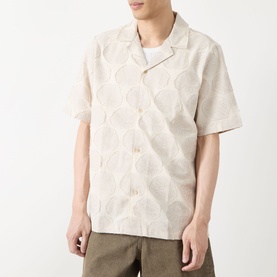 Model wearing Les Deux Dahlia Jacquard Shirt in light sand with floral medallion pattern, camp collar, short sleeves, styled with khaki trousers.
